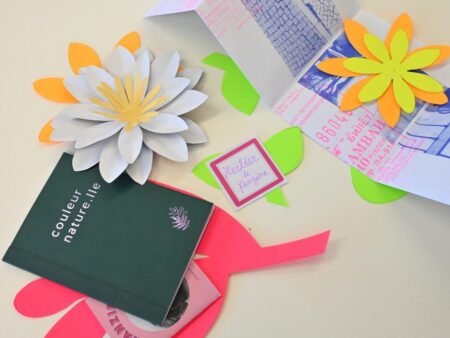 Un herbier et des fleurs en papier sont disposées sur une table. Il est écrit "Herbier & Fanzine" sur une étiquette au milieu.